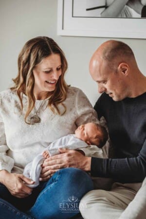 parents sit on a bed and hold their baby girl between them