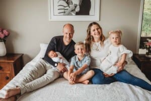 A family sits on a bed holding their newborn baby