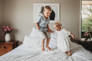 Small siblings jump on a white bed laughing