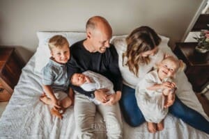 A family sits on a bed holding their newborn baby