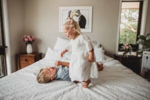 2 small children jump on a white bed