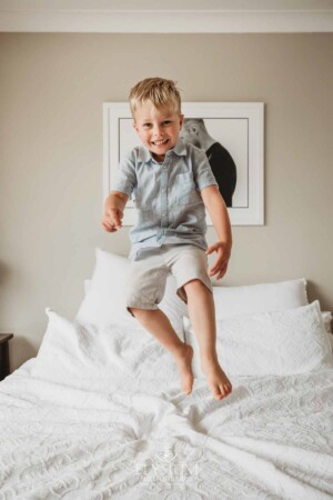 A little boy jumps on a white bed
