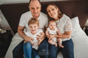 Newborn Photography: parents sit on a bed and cuddle their children in their laps