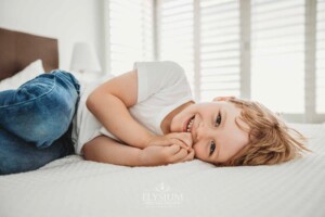 Newborn Photography: a little boy lays on a white bedspread smiling
