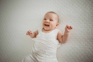 Newborn Photography: a baby girl lays in a white wrap and smiles