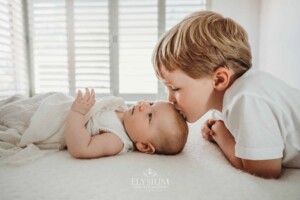 Newborn Photography: a little boy leans over his baby sister and kisses her forehead
