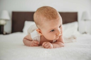 Newborn Photography: a baby girl lays on her tummy on a white bedspread