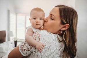 Newborn Photography: a mother holds her baby girl on her shoulder and kisses her cheek