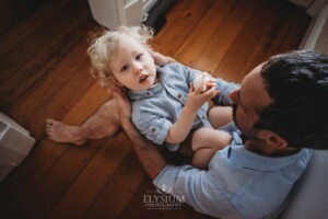 Newborn Photography: a father sits cradling his baby boy in his lap