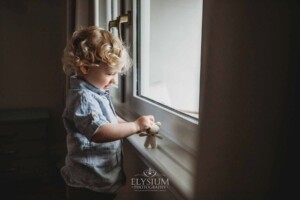 Newborn Photography: a little boy plays with a teddy bear on a windowsill