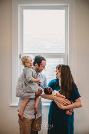 Newborn Photography: parents hold their baby boys in front of a window