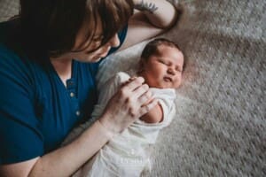 Newborn Photography: a mother lays on a white blanket with her baby boy