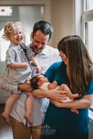 Newborn Photography: a little boy laughs as he is held by his parents