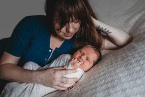 Newborn Photography: a mother lays on a white blanket with her baby boy