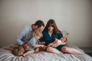 Newborn Photography: parents sit with their baby boys on a bed