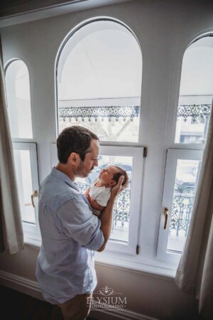 Newborn Photography: a father holds his baby boy in front of a bright window