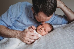 Newborn Photography: a father lays on a white blanket with his baby boy