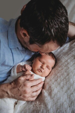 Newborn Photography: a father lays on a white blanket with his baby boy
