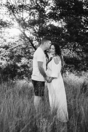 Outdoor Session - a man kisses his pregnant wife who wears a white dress