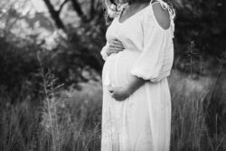 Outdoor Session - a pregnant woman in a white maternity dress holds her belly