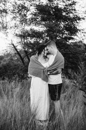Outdoor Session - a man hugs his pregnant wife with a blanket wrapped around them