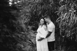 Outdoor Session - a pregnant woman in a white maternity gown leans into a man