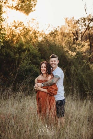 A man hugs his pregnant wife in a long linen maxi dress