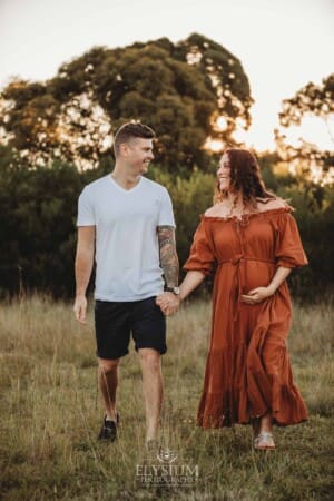 Outdoor Session - a man walks with his pregnant wife through long grass at sunset