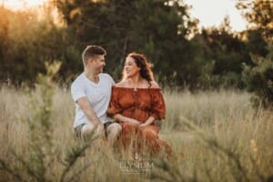 Outdoor Session - a couple sit in long grass as the sun sets behind them