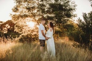 Outdoor Session - a couple hold hands standing in long grass with the sunset behind them