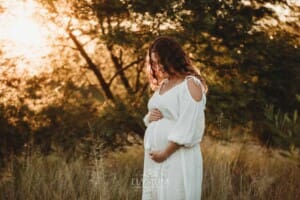 Outdoor Session - a pregnant woman in a white maternity dress stands in long grass