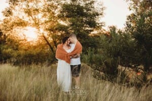Outdoor Session - a man hugs his pregnant wife with a blanket wrapped around them