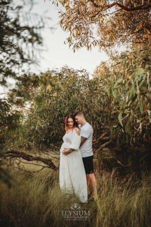 Outdoor Session - a man hugs his wife and places his hand on her pregnant belly
