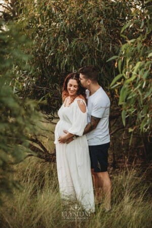 Outdoor Session - a man kisses his pregnant wife on the head
