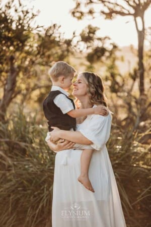 A pregnant mother rubs noses with her child as she cuddles him at sunset on a beach