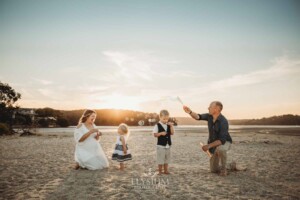 A family plays with bubbles to entertain their kids on a sandy beach at sunset