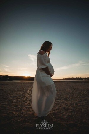 Silhouette of a pregnant woman standing on a beach with the orange glow of sunset behind her