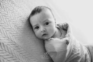 A newborn baby lays wrapped on a white blanket