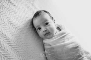 A newborn baby lays wrapped on a white textured blanket