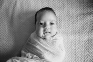 A newborn baby lays wrapped on a white textured blanket