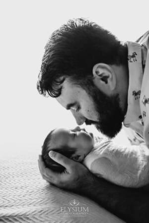 A father holds one of his newborn twins in his hands laying on a white blanket