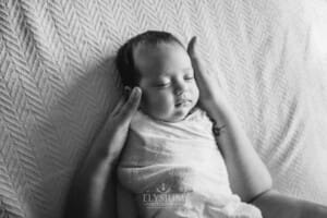 A mother holds one of her newborn twins in her hands as she lays on a white textured blanket