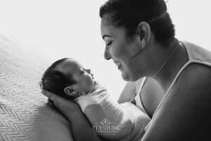 A mother holds one of her newborn twins in her hands laying on a white blanket