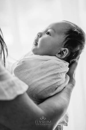 A newborn baby looks up at his mother in her arms wrapped in white