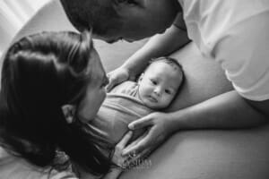 Parents hold their newborn baby boy in their hands as he lays on a blanket