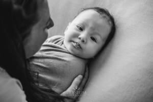 A mother holds her newborn baby boy laying on a blanket, black and white photograph