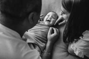 Parents hold their newborn baby boy in their hands as he lays on a blanket