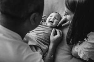 Parents hold their newborn baby boy in their hands as he lays on a blanket