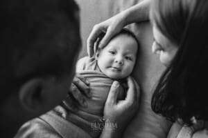 Parents hold their newborn baby boy in their hands as he lays on a blanket