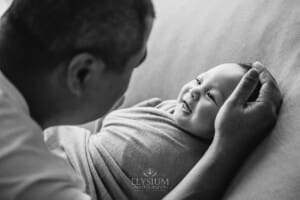 A newborn baby giggles as he lays in his father's hands with his dad leaning over him